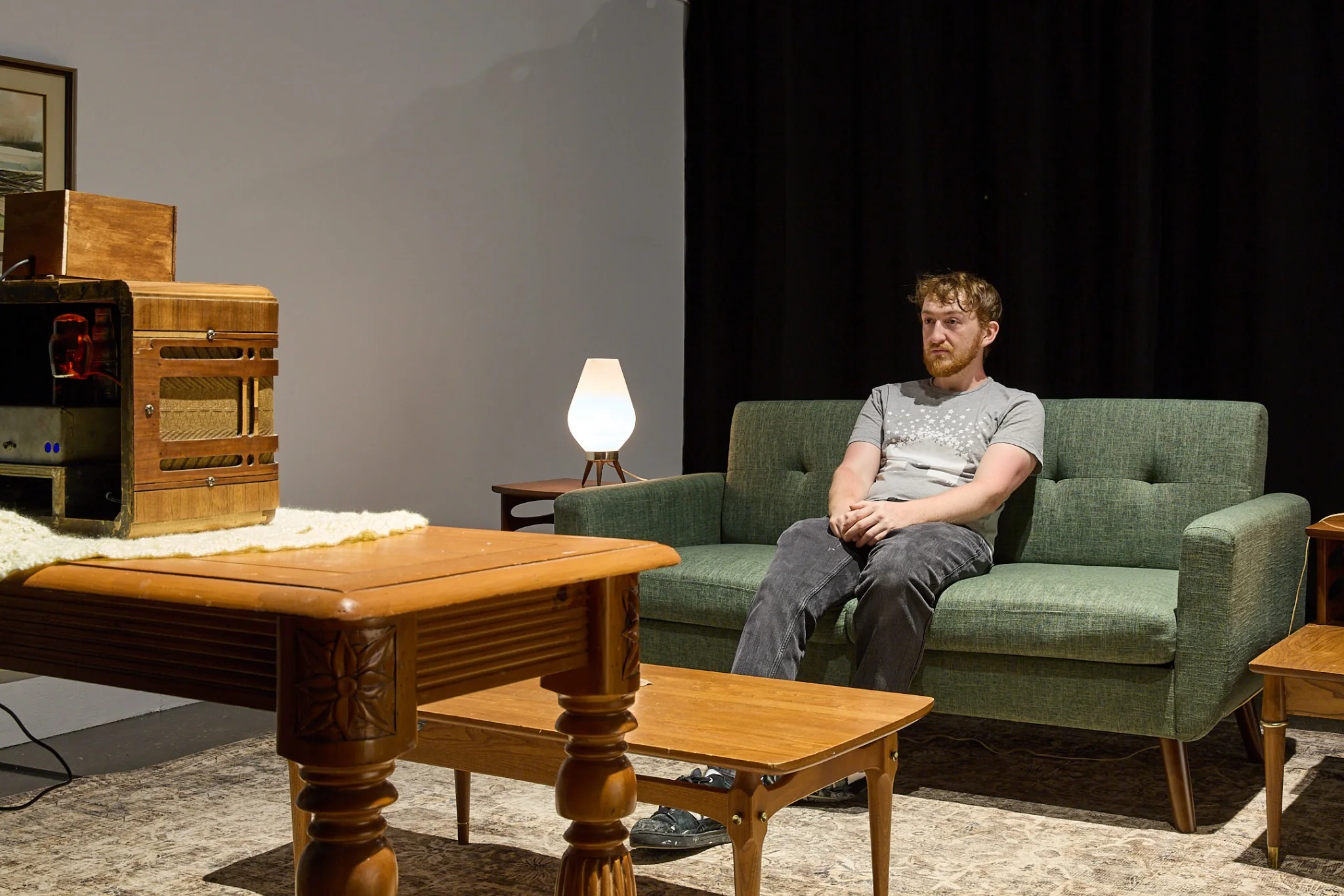 Visitor seated on a green sofa facing the Victory Box in the living room installation